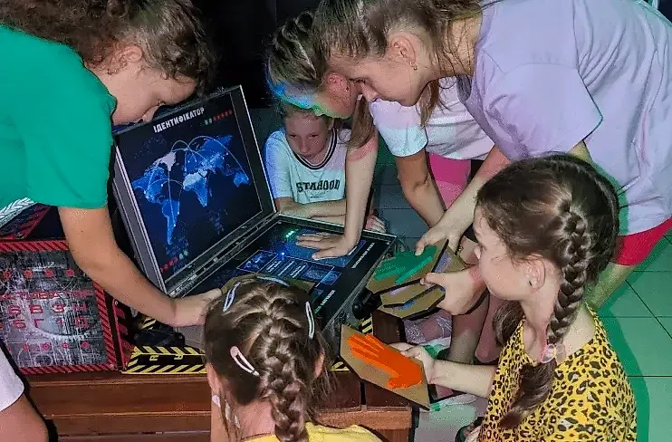 Біля інтерактивної валізи з картою та написом «ІДЕНТИФІКАТОР» зібралися шестеро дівчат і підлітків: ліворуч учасниця в зеленій футболці тримає панель, а в центр